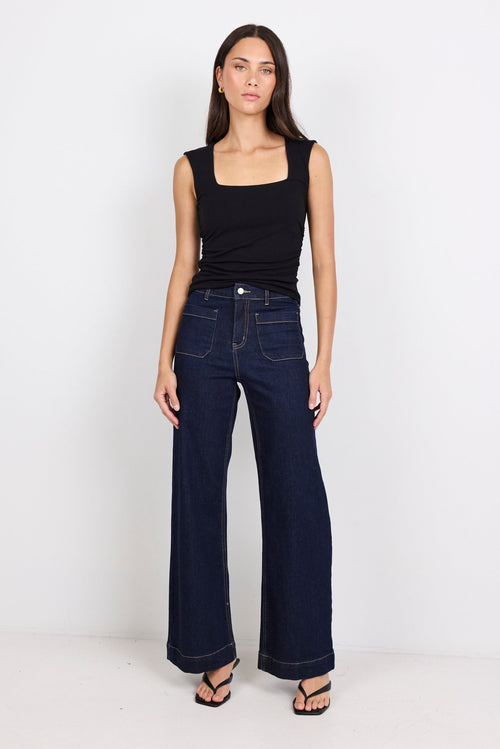 Woman wearing a black sleeveless top and dark blue jeans on a white background