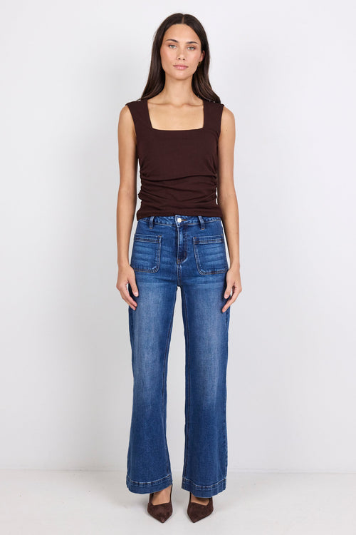 Woman wearing a brown top and blue jeans on a white background