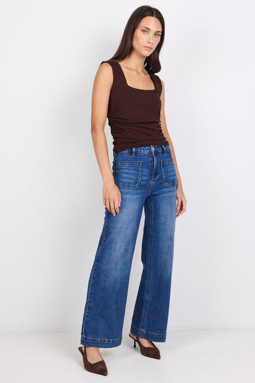Woman wearing blue jeans and a brown top on a white background