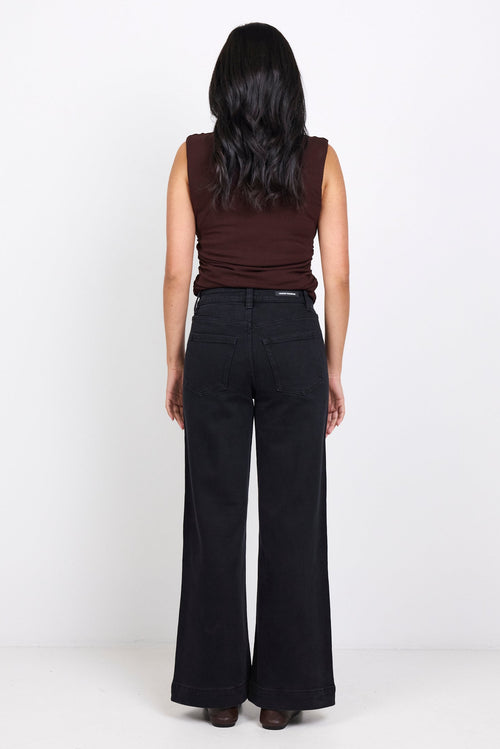Person wearing a brown sleeveless top and black wide-leg pants on a white background