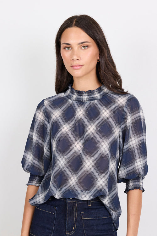 Woman wearing a blue and white plaid blouse with dark jeans on a white background
