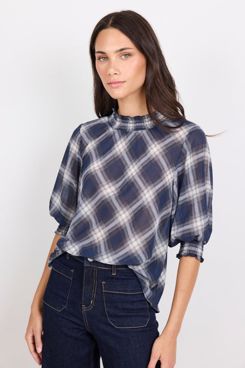 Woman wearing a blue plaid shirt and dark jeans on a white background