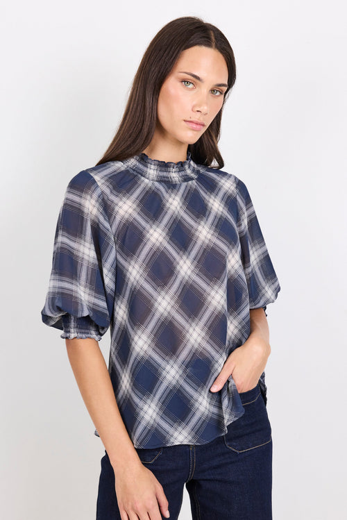 Woman wearing a blue and white checkered blouse with puffed sleeves on a white background