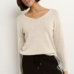 Woman wearing a natural beige V-neck jumper with black drawstring pants featuring white side stripes.