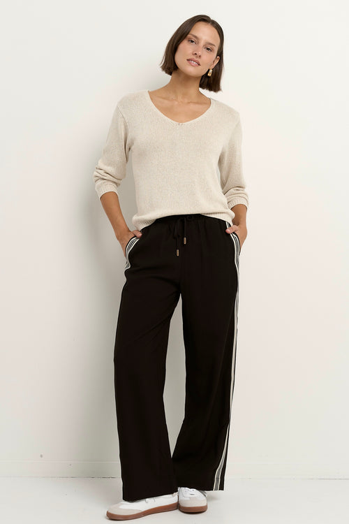 Woman wearing a natural beige V-neck jumper with black drawstring pants featuring white side stripes.