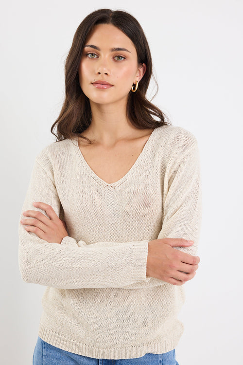 Woman wearing a beige sweater and blue jeans against a white background