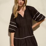 Woman wearing a black mini dress with tiered skirt, white scalloped trim, and puff sleeves.