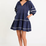 Model wearing a navy tiered short sleeve smock dress with a relaxed fit and contrast trim detail.
