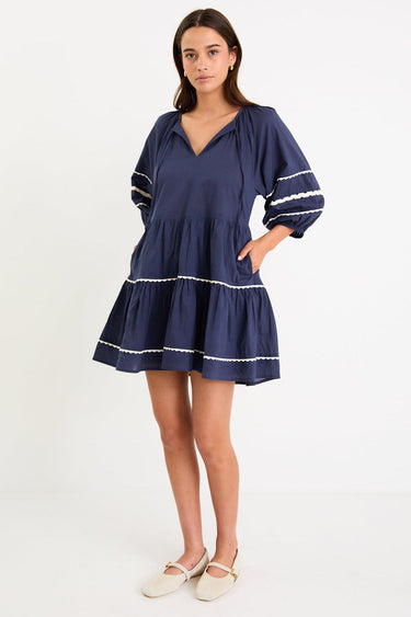 Model wearing a navy tiered short sleeve smock dress with a relaxed fit and contrast trim detail.