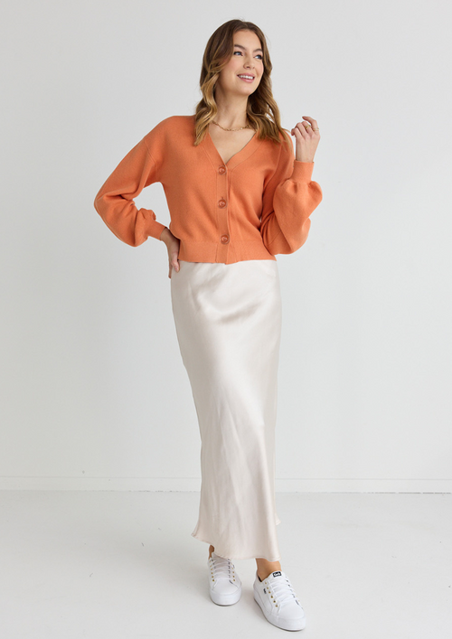 model wears orange cardigan and long white satin midi skirt and white sneakers