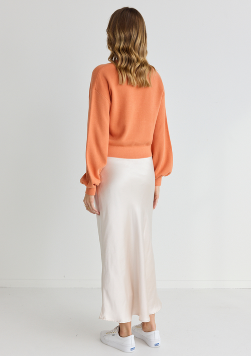 model wears orange cardigan and long white satin midi skirt and white sneakers