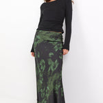 Woman wearing a black top and green patterned skirt on a white background