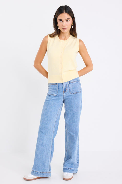Woman wearing a sleeveless yellow vest with button-down front and crew neck, paired with blue jeans.