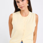 Woman wearing a sleeveless yellow vest with button-down front and crew neck, paired with blue jeans.