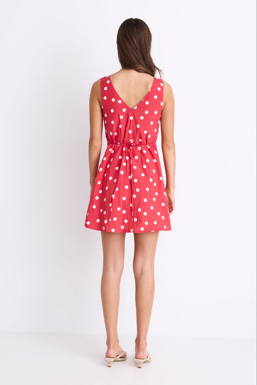 model wearing a red white polka dot mini dress with a V neck and button front