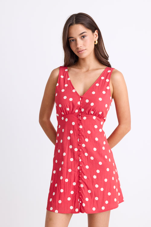 model wearing a red white polka dot mini dress with a V neck and button front