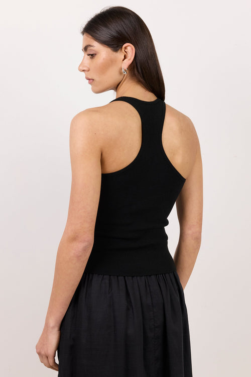 A woman shown from the back wearing a black sleeveless racerback tank top and a black skirt, photographed against a plain light background.