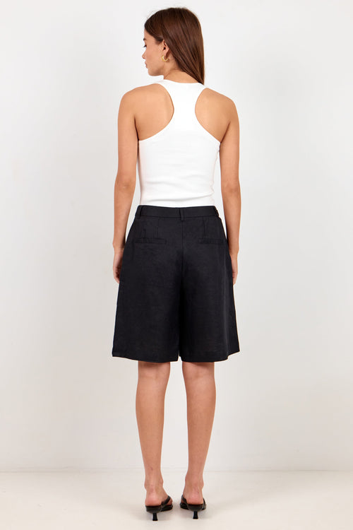 A woman is shown from the back wearing a white halter-neck tank top and black wide-leg shorts, standing against a plain white studio background.
