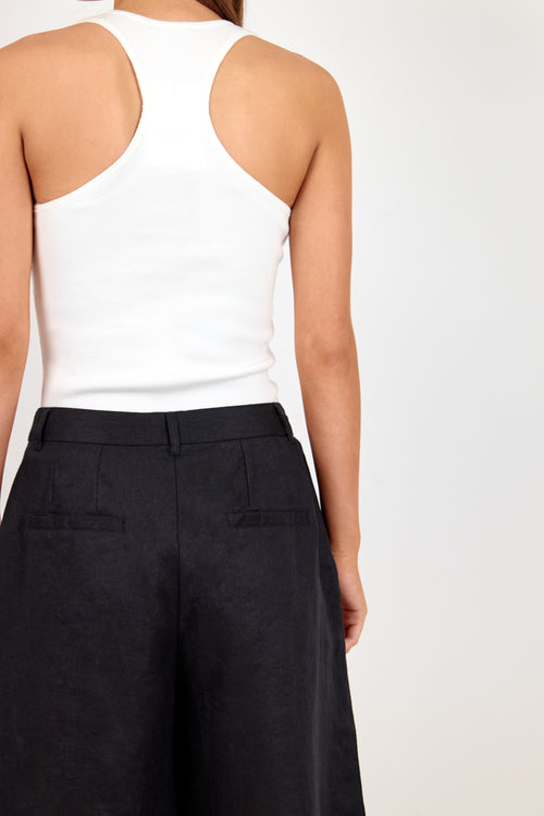 Rear view of a model wearing a white ribbed racerback tank top and black wide-leg shorts against a light gray studio background.