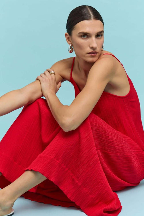Bright red textured maxi dress with thin spaghetti straps and a deep V-neckline, styled in a relaxed fit, worn by a model against a neutral background.