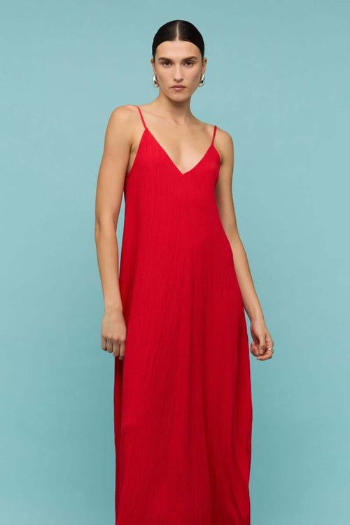 Bright red textured maxi dress with thin spaghetti straps and a deep V-neckline, styled in a relaxed fit, worn by a model against a neutral background.