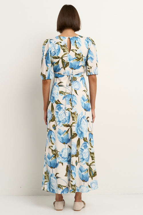 Woman wearing a short sleeve floral midi dress with a V-neck and blue rose print on a cream base.