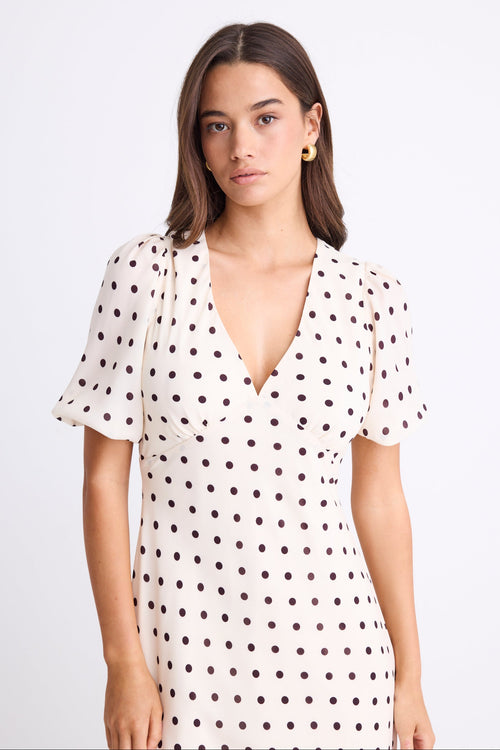Woman wearing a cream midi dress with chocolate polka dots, V-neckline, short puff sleeves, and a flattering bias-cut silhouette.