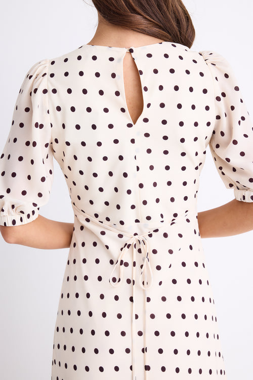 Woman wearing a cream midi dress with chocolate polka dots, V-neckline, short puff sleeves, and a flattering bias-cut silhouette.