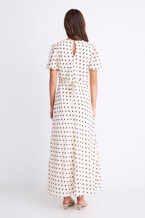 Woman wearing a cream midi dress with chocolate polka dots, V-neckline, short puff sleeves, and a flattering bias-cut silhouette.
