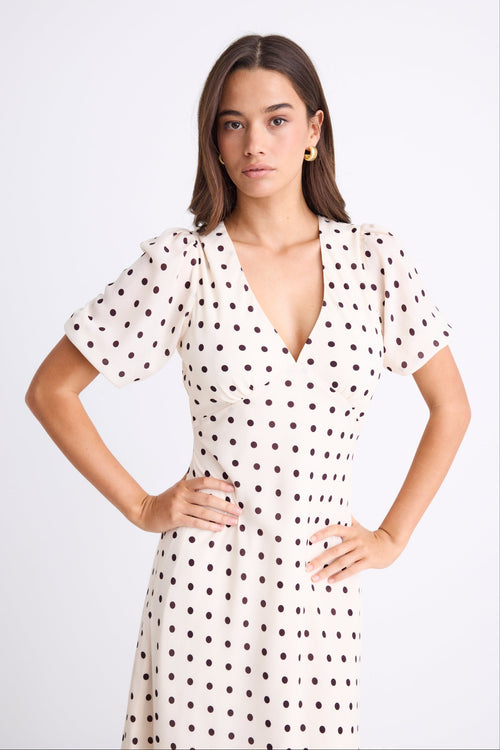Woman wearing a cream midi dress with chocolate polka dots, V-neckline, short puff sleeves, and a flattering bias-cut silhouette.