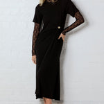 Woman wearing a black dress with lace sleeves against a white wall