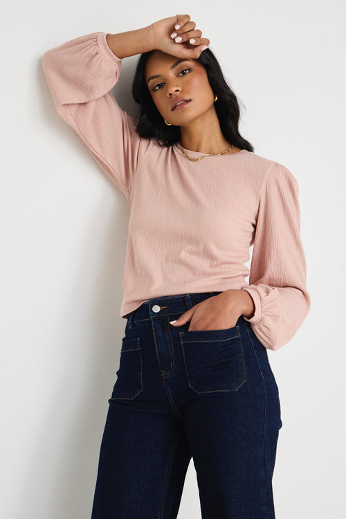 Model wears a blush pink top with jeas