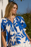 Woman wearing a blue and white floral blouse standing outdoors.