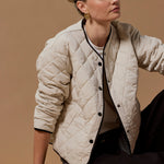 Woman wearing a beige quilted jacket sitting on a brown background