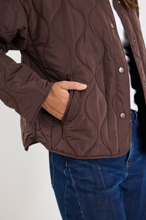 Brown quilted jacket with a person wearing it on a plain background