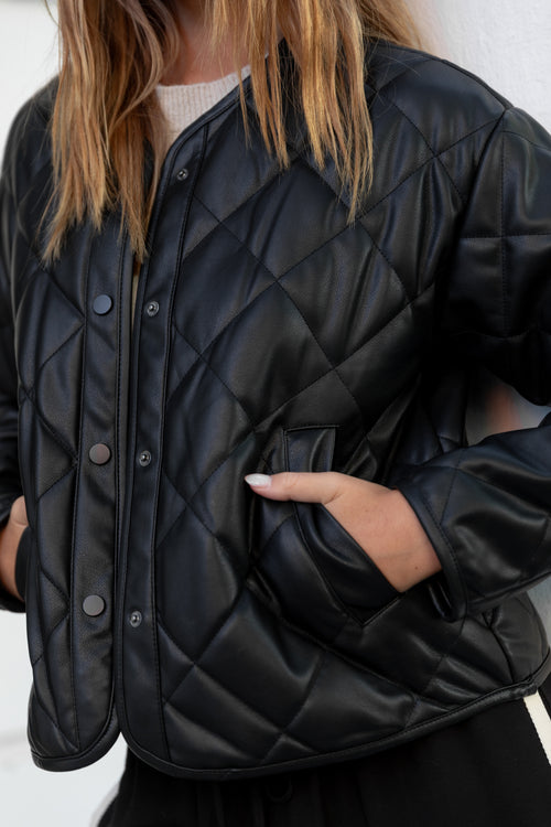 Person wearing a black quilted jacket with a plain background
