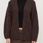 Person wearing a brown cardigan and pants on a white background