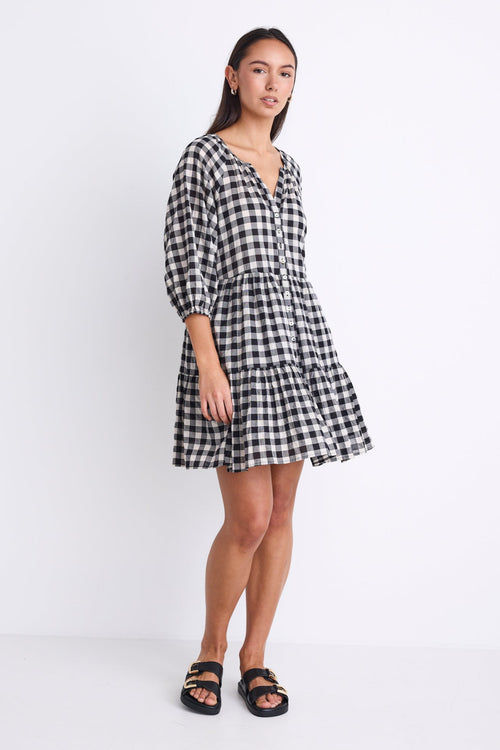 Woman wearing a black and white gingham mini dress with a button-down front, tiered skirt, and mid-length sleeves.