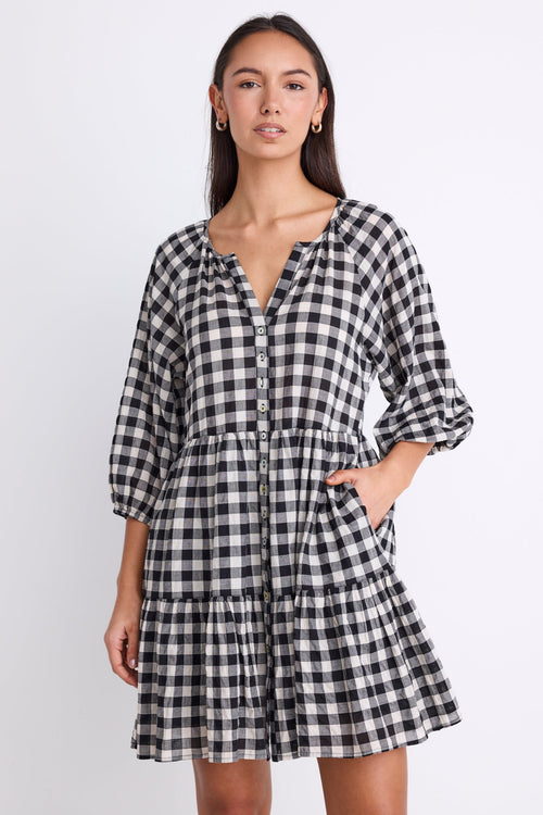 Woman wearing a black and white gingham mini dress with a button-down front, tiered skirt, and mid-length sleeves.
col_pattern