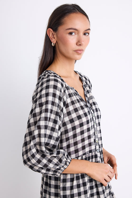 Woman wearing a black and white gingham mini dress with a button-down front, tiered skirt, and mid-length sleeves.