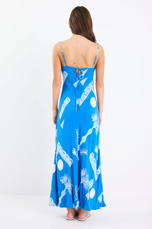 Woman wearing a bright blue strappy bias-cut slip midi dress with white palm and geometric print, relaxed fit, and fluid drape.
