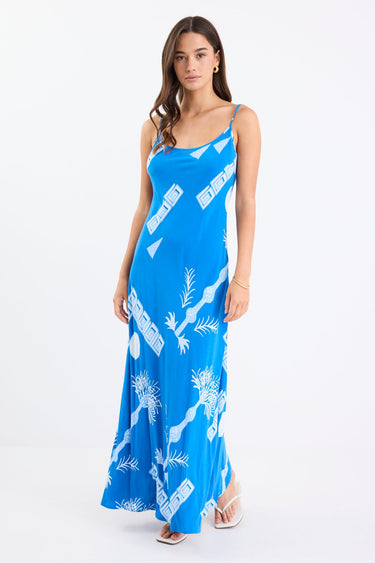 Woman wearing a bright blue strappy bias-cut slip midi dress with white palm and geometric print, relaxed fit, and fluid drape.