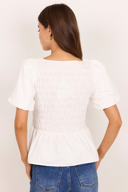 A woman viewed from the back wearing a white smocked blouse with short puff sleeves and blue jeans, standing against a plain light background.
col_pattern
