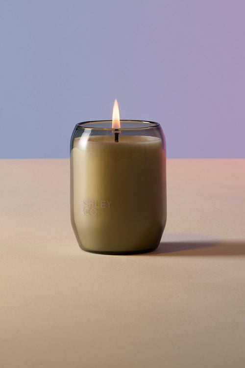 Candle in a glass jar with a lit wick on a gradient background