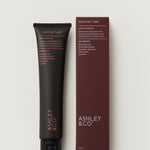Black tube and maroon box of Ashley & Co hand cream on a light gray background