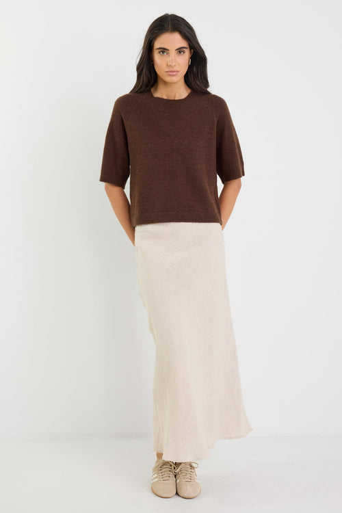 Woman wearing a brown top and beige skirt on a white background