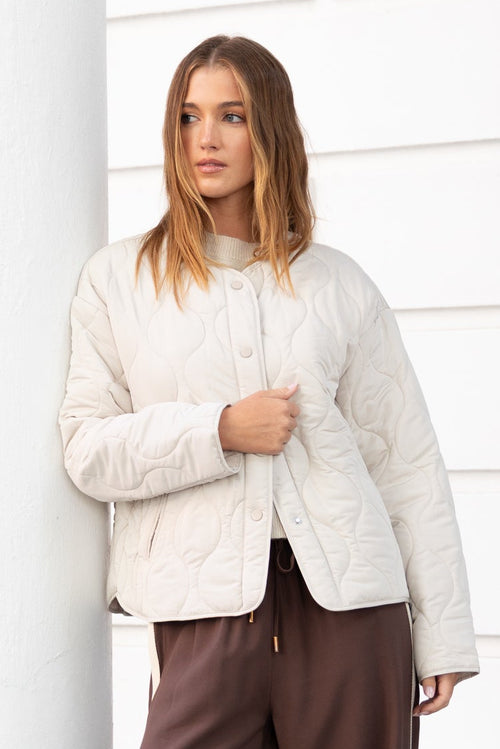 Woman in a white sweater and brown pants standing on a white building steps.