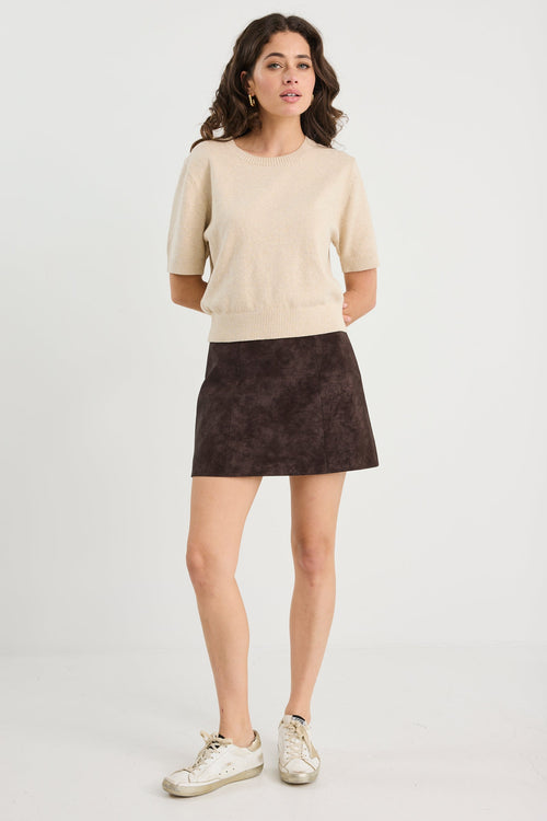 Woman wearing a beige sweater and dark skirt on a white background