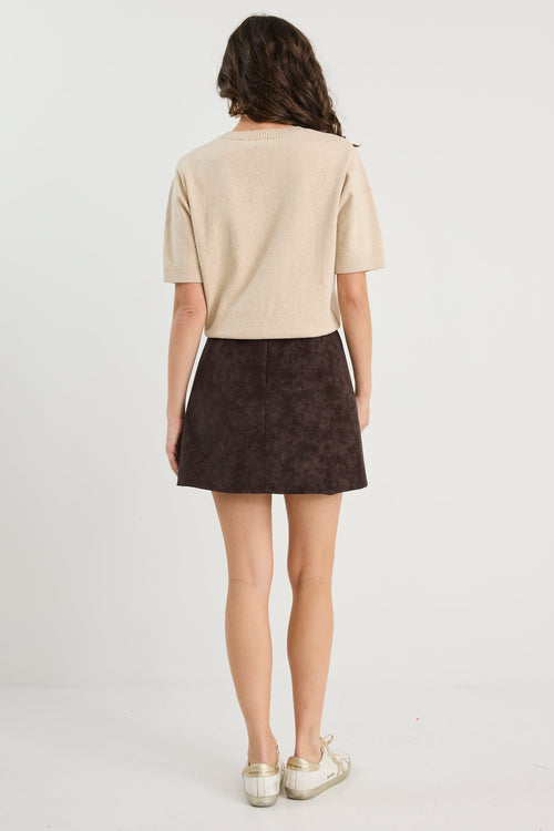 Person wearing a beige top and brown skirt on a white background