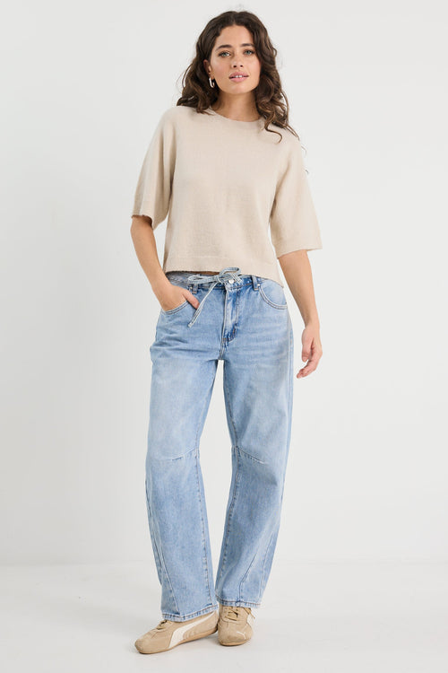Woman wearing a beige sweater and light blue jeans on a white background